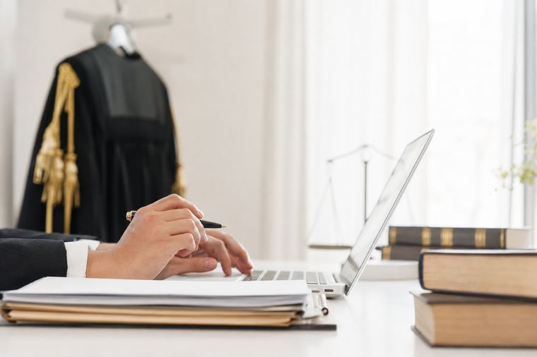 Una donna in maglia scura lavora al portatile argentato appoggiato sul piano di lavoro